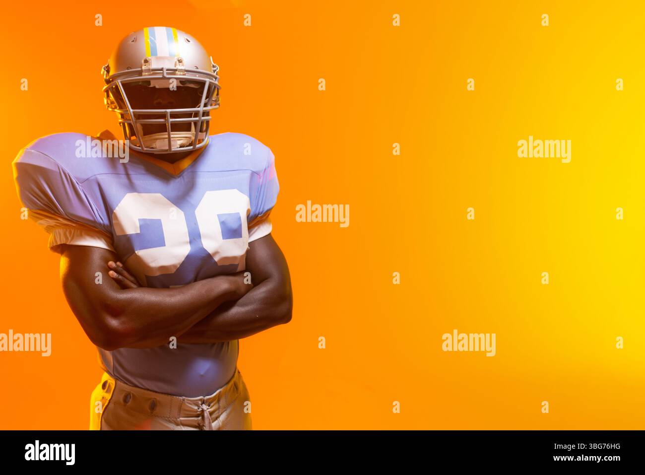Fußballspieler, der im Studio vor orangefarbenem Hintergrund steht, Trikot Nr. 99 und Helm trägt Stockfoto