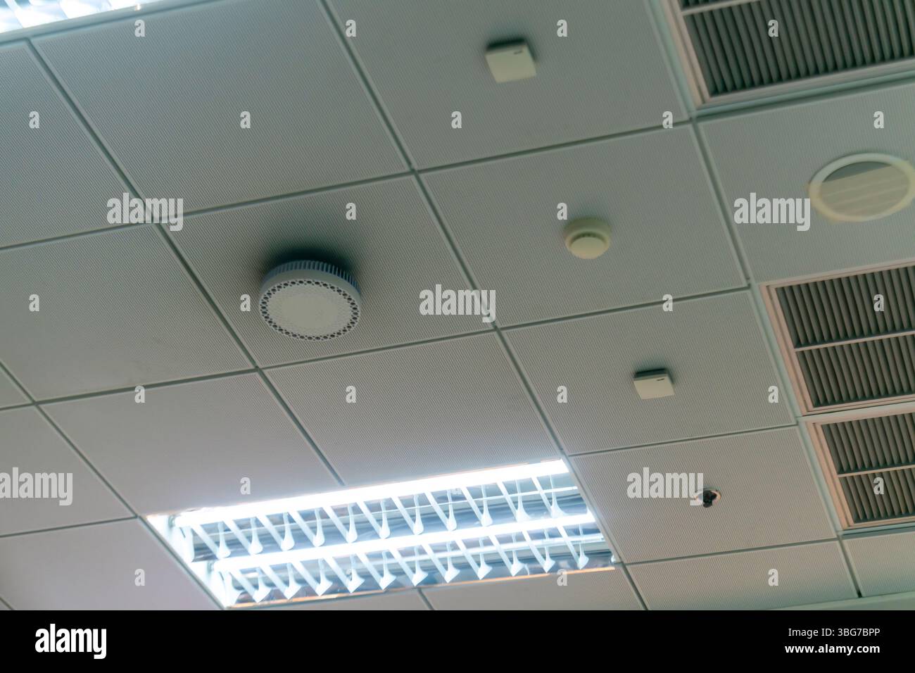 Modernes Deckendesign für Büros mit Deckenleuchten und Sensoren. Die klaren Linien und die minimalistische Ästhetik verbessern das Arbeitsumfeld und verbessern die Arbeitsumgebung Stockfoto