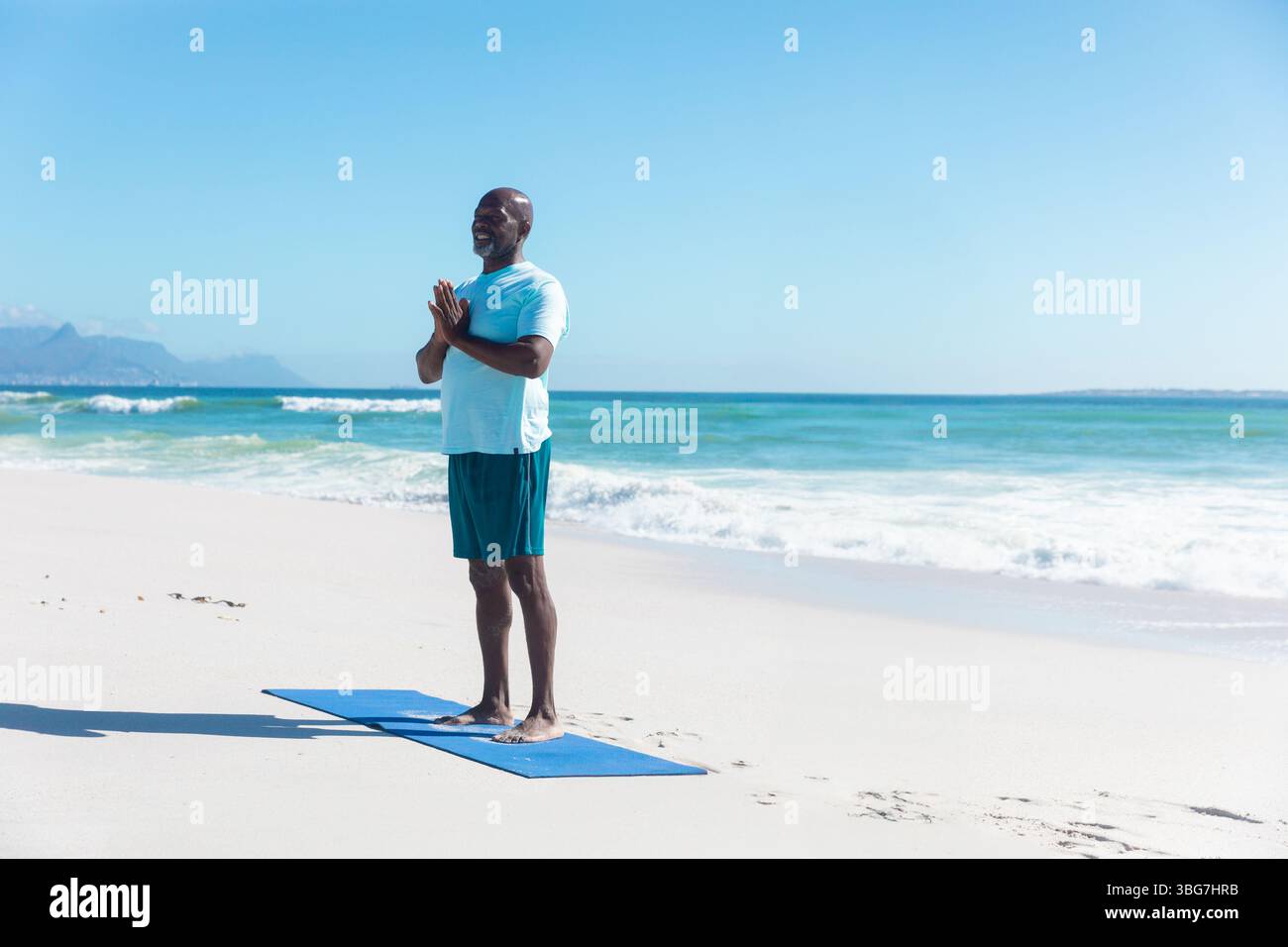 Ranghoher Afroamerikaner in Sportbekleidung, der Pose auf blauer Yogamatte am Strand hält, Kopierraum Stockfoto