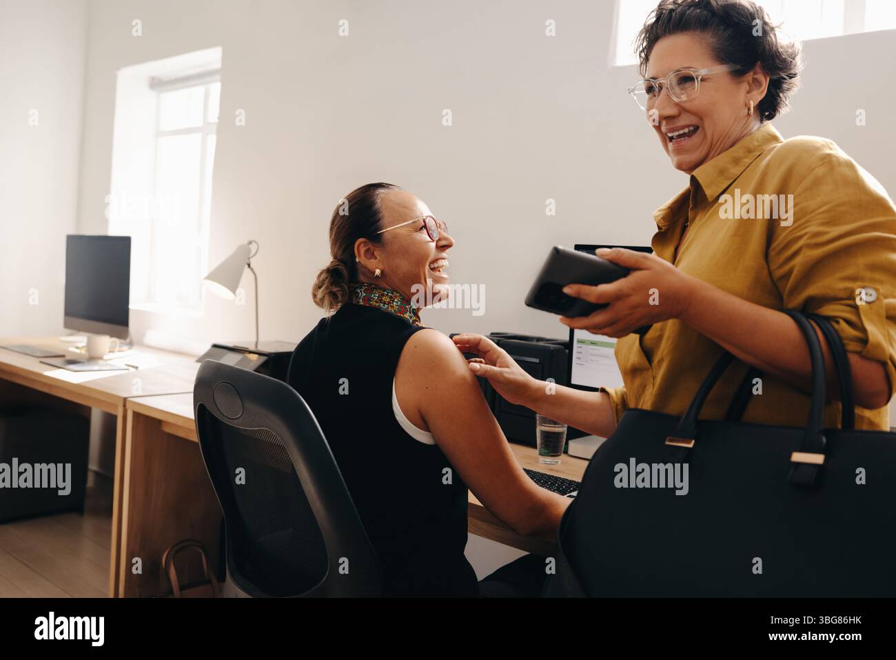 Zwei Kollegen teilen einen freudigen Moment, während sie in einer modernen Büroumgebung zusammenarbeiten, um ein Gefühl von Kameradschaft und Teamarbeit zu spüren. Stockfoto