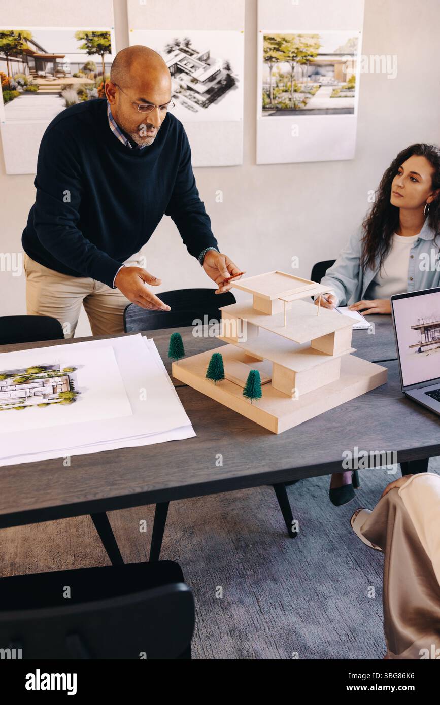 Fachleute in einer modernen Büroumgebung diskutieren gemeinsam Architekturentwürfe und Baupläne anhand eines maßstabsgetreuen Modells und gedruckter Matte Stockfoto