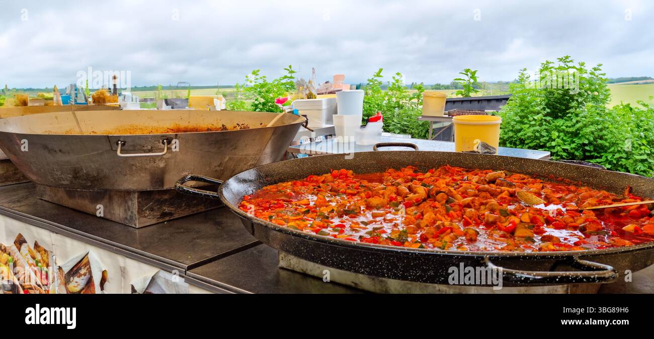 Market Amboise, Frankreich - 23.5,2025: Kochen im Freien mit großen Eisenpfannen mit Eintopf, Tomatosausage und Penne Nudeln Stockfoto