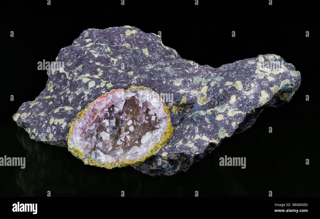 Wunderschöne Kristall-Edelsteinkristalle in gebrochener Achatgeode in Melaphyrstein auf schwarzem Hintergrund. Vulkanische Magmatische Gesteinsprobe mit kleinen grünen Knoten. Stockfoto