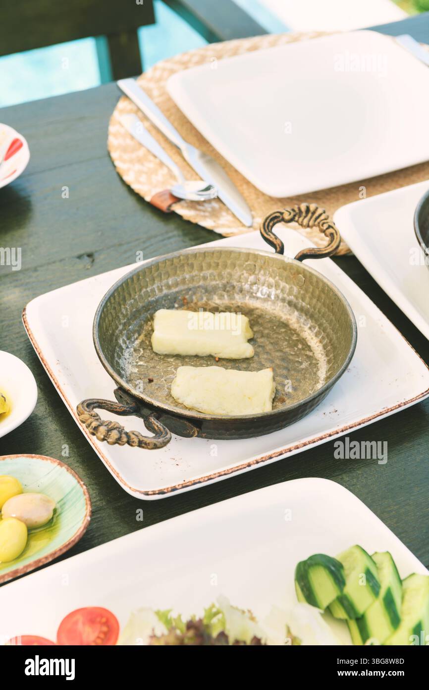 Eine köstliche Nahaufnahme des goldenen halloumi-Käses, der in einer traditionellen Kupferpfanne vom Frühstücksangebot brutzelt. Stockfoto