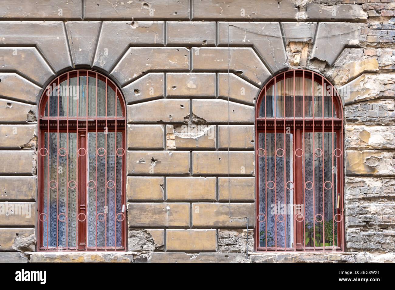 Strukturierter Hintergrund aus alten Ziegelmauern mit Kugeln und Muschelspuren aus dem Krieg und zwei Bogenfenster mit Gittern Stockfoto