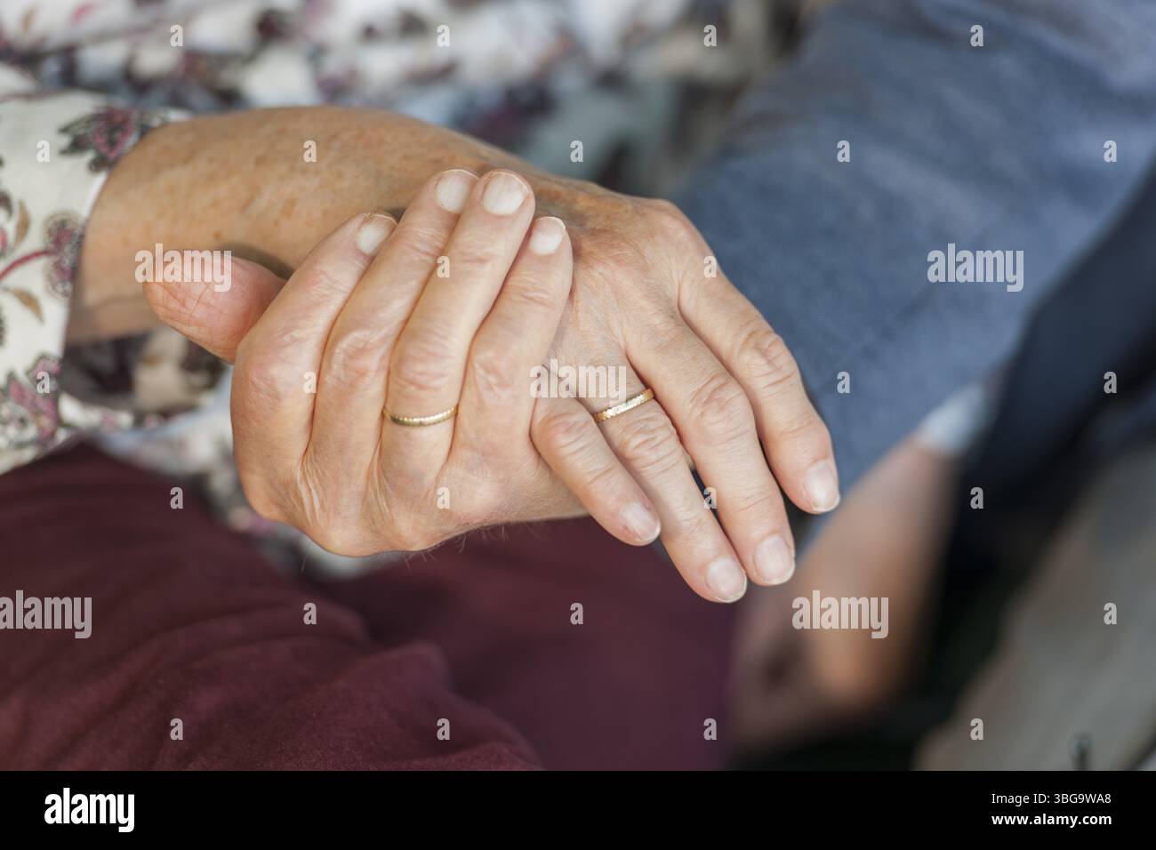 Nahaufnahme des Handhaltens eines 80-jährigen Ehepaares mit Eheringen Stockfoto