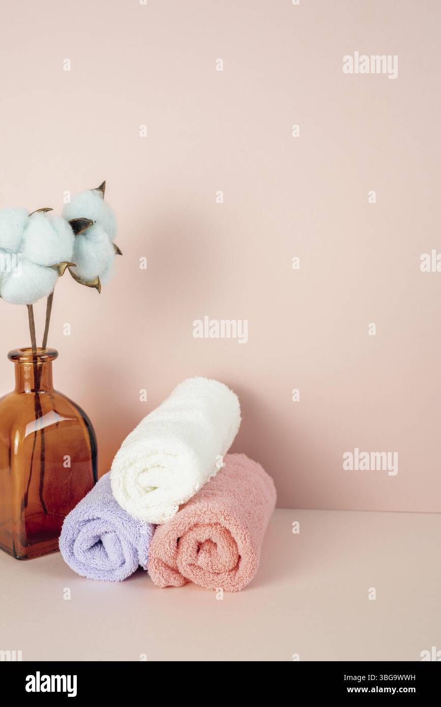 Weiches, sauberes Handtuch im Badezimmer mit Blumenvase aus Baumwolle auf einem rosafarbenen Tisch. Rosafarbener Wandhintergrund. Speicherplatz kopieren Stockfoto