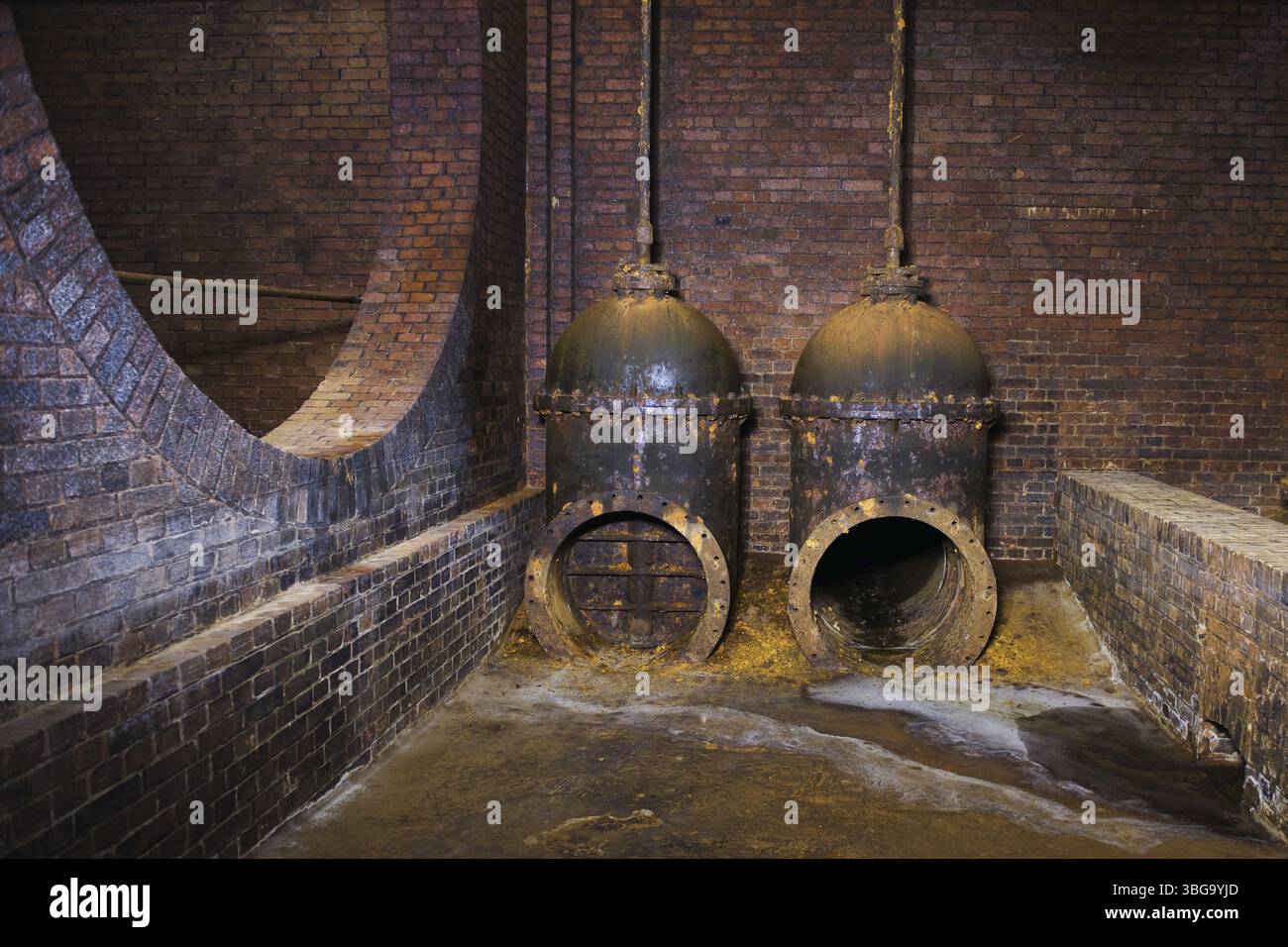 Weitwinkelansicht zweier alter Wasserrohre im unterirdischen Ziegelgewölbe Stockfoto