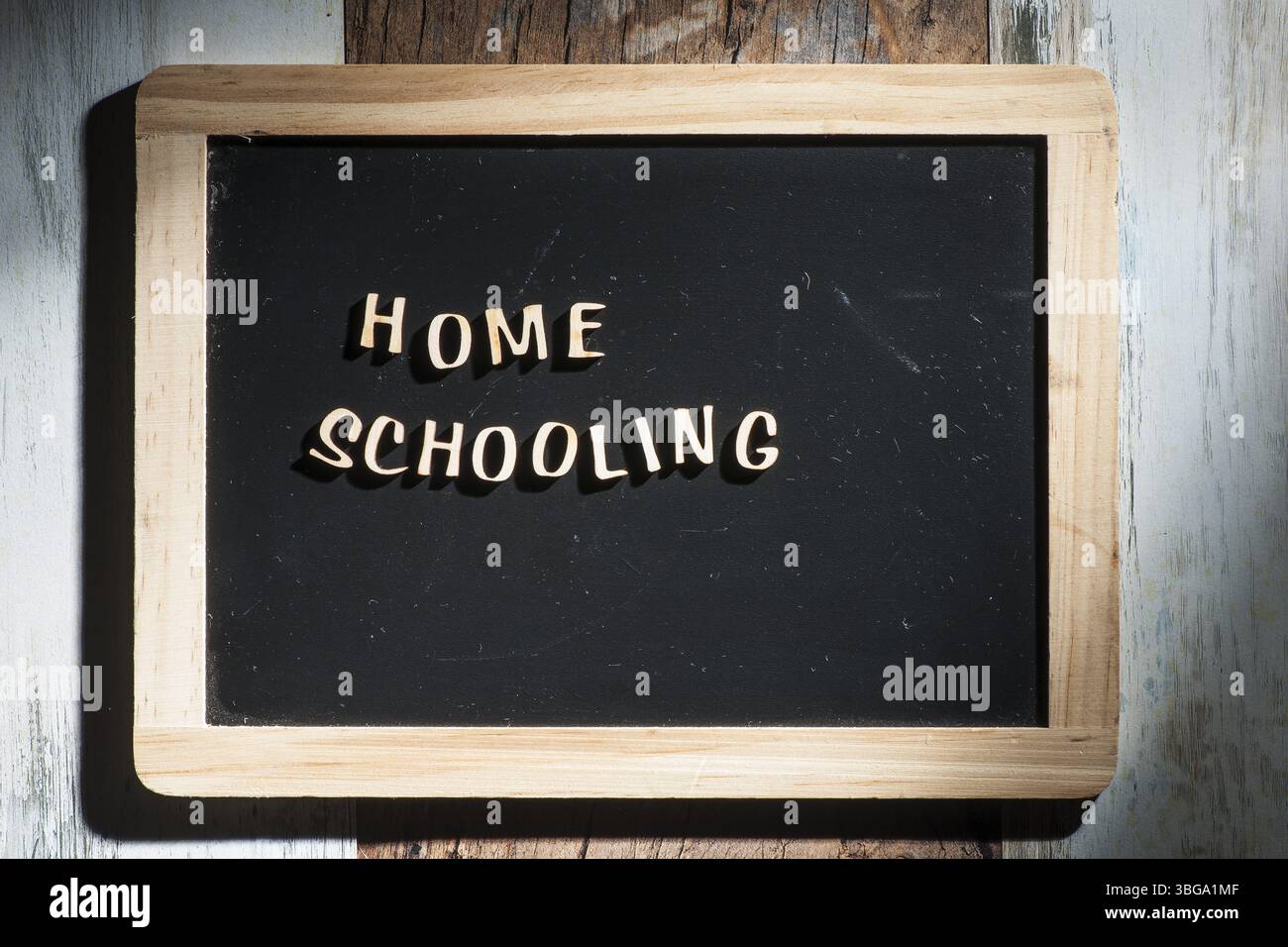 Frontale Nahaufnahme eines kleinen schwarzen Kreidebretts aus Holzbuchstaben mit den Worten Home School auf einer Holzfläche im rauen Seitenlicht Stockfoto