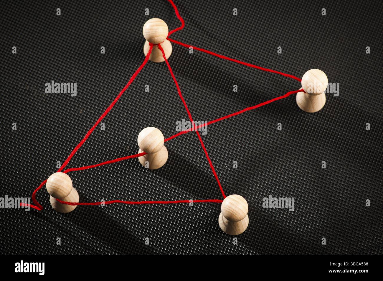 Erhöhte Detailansicht von Ludo-Spielstücken, verbunden mit rotem Faden auf dunklem, genopptem Hintergrund in rotem und blauem Seitenlicht Stockfoto