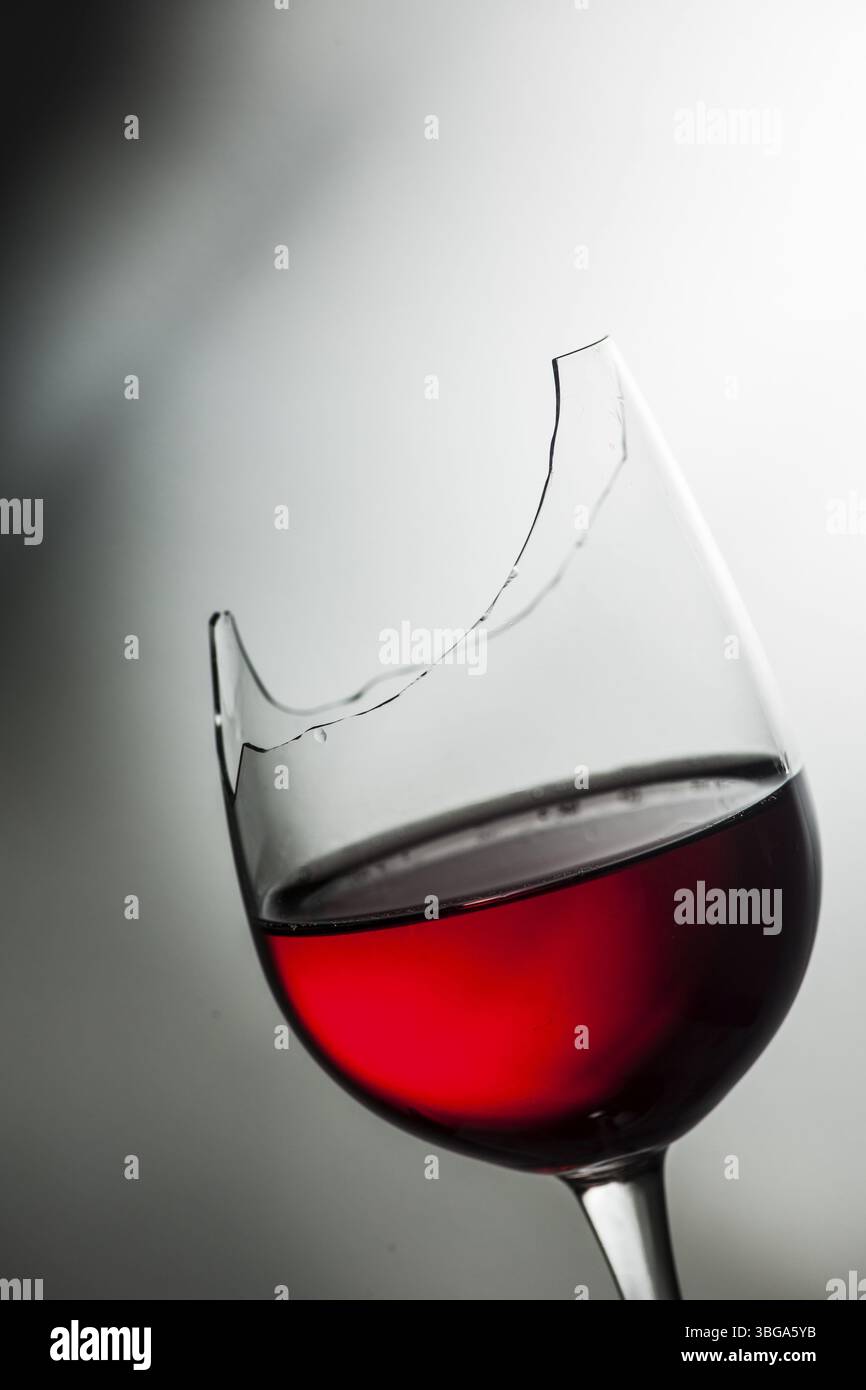 Studio-Aufnahme von der Oberseite eines gebrochenen Weinglases gefüllt mit Rotwein vor einem strukturierten Hintergrund mit hellem und dunklem Farbverlauf Stockfoto