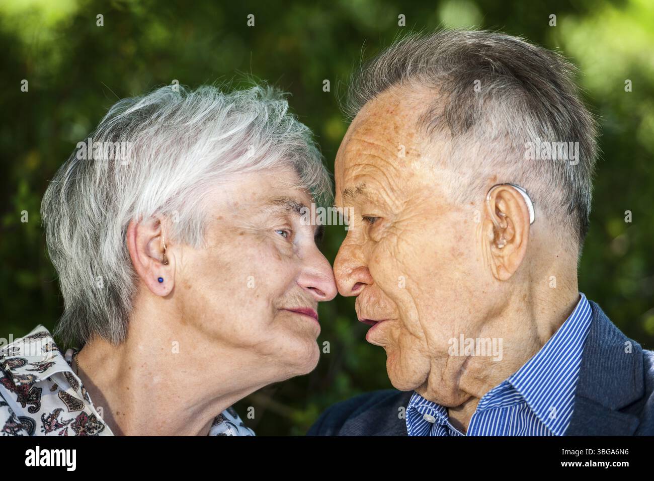Kopf-Schulter-Porträt eines älteren Rentnerpaares mit Brille vor grünen Blättern im Sommer, der fröhlich in die Kamera blickt Stockfoto
