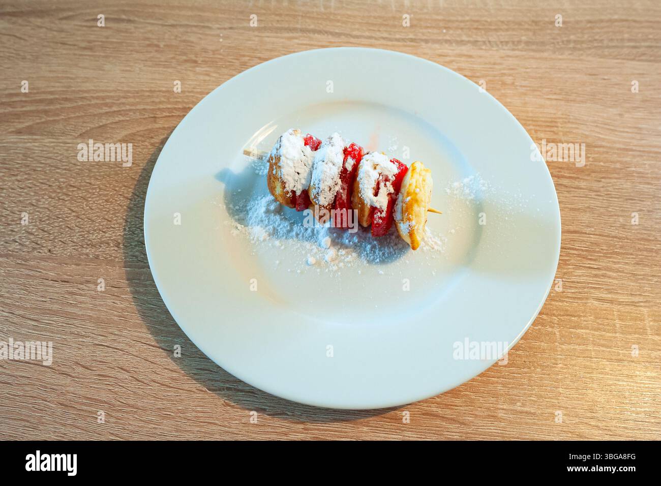 Teller mit traditionellen niederländischen Teigkuchen und Erdbeerscheiben auf einem Stock, bestreut mit Puderzucker Stockfoto