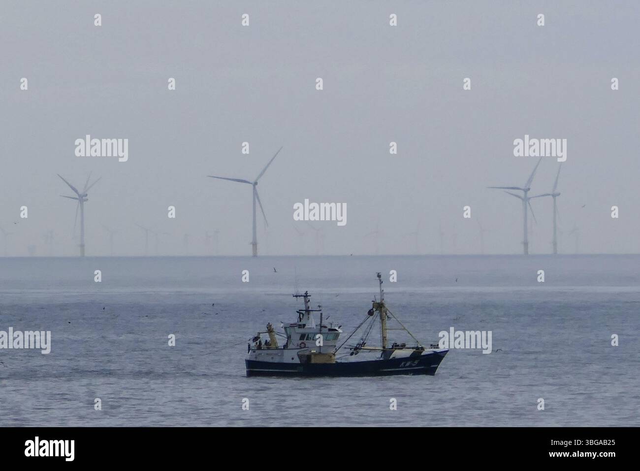 Fischerboot im Hintergrund einer Windturbine am See Stockfoto
