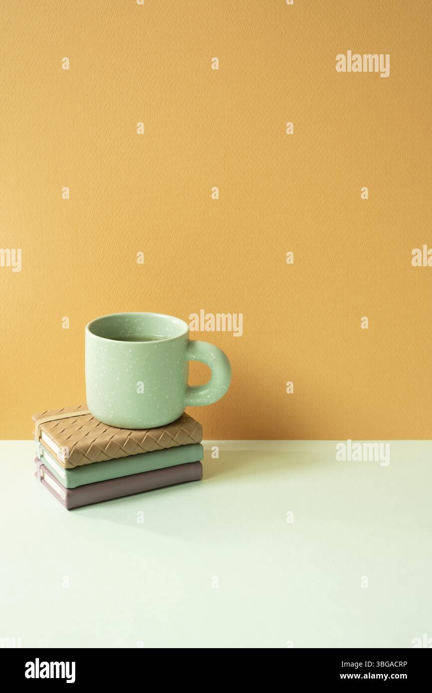 Stapel Notebook und Becher auf minzgrünem Schreibtisch. Orangefarbener Hintergrund. Leerzeichen kopieren Stockfoto