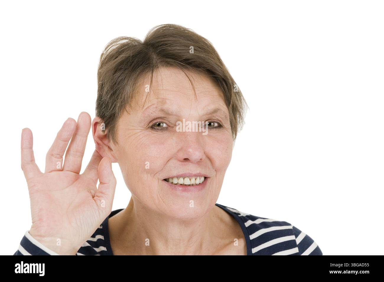 Kopf-und-Schultern-Ansicht einer Reifen Frau in einem gestreiften Hemd, die Hand am rechten Ohr hält und freundlich in die Kamera vor einem weißen Ba blickt Stockfoto
