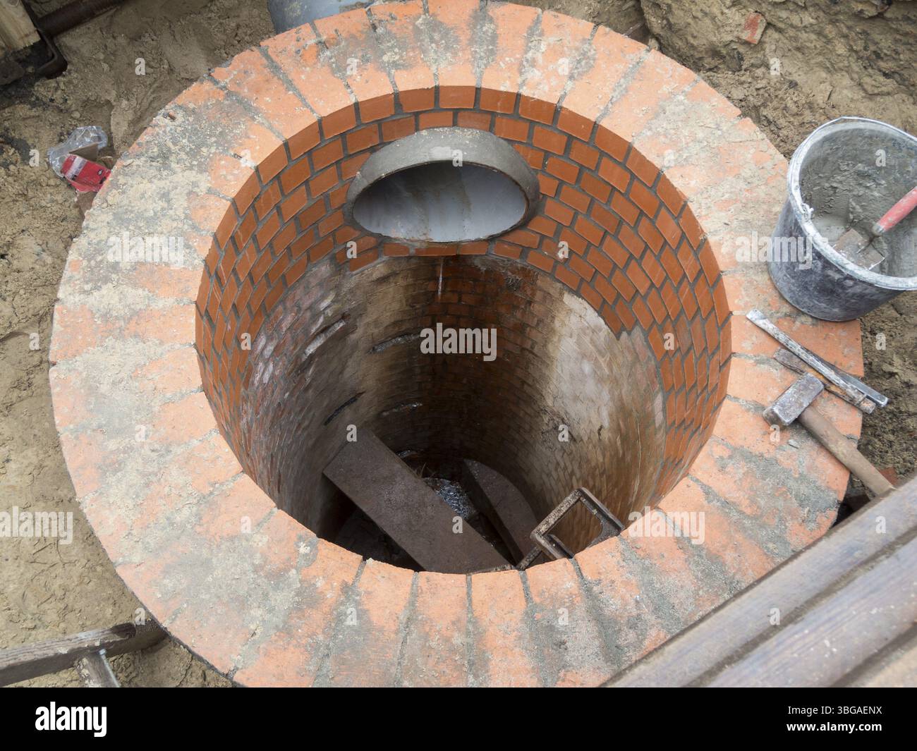 Erneuerung eines kreisförmigen Abwasserschachts mit Ziegeln in der Hülle in einer offenen Grabungsgrube Stockfoto