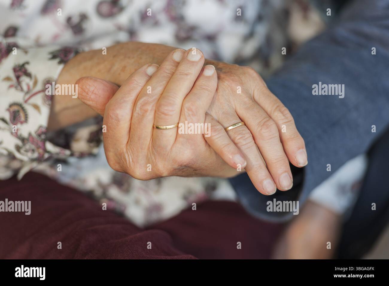 Nahaufnahme des Handhaltens eines 80-jährigen Ehepaares mit Eheringen Stockfoto