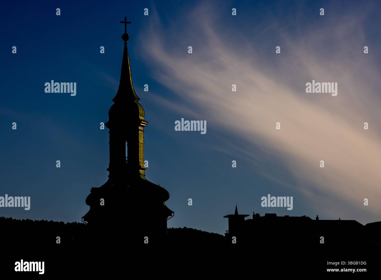 Ein mit Silhouette versehener Kirchturm und Dächer mit Hinterleuchtung bei Sonnenuntergang und dramatischer Wolkenlandschaft, in Bergen, Norwegen, bei Sonnenuntergang. Stockfoto