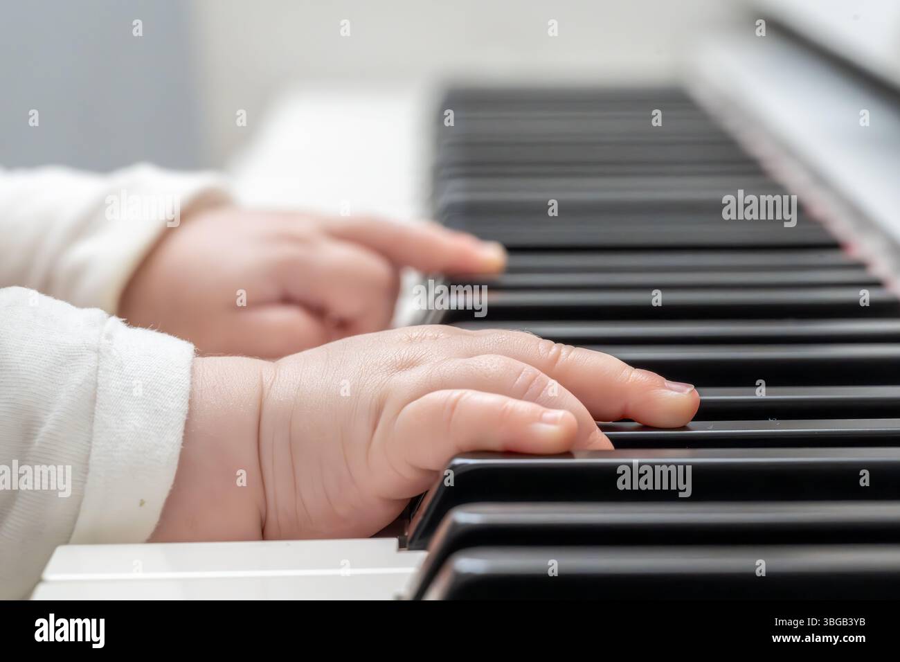 Beschreibung: Super Nahaufnahme der Hand eines Babys in einem weißen Pullover, der das Klavier in einer hellen Umgebung spielt. Junges Leben und Musik. Stockfoto