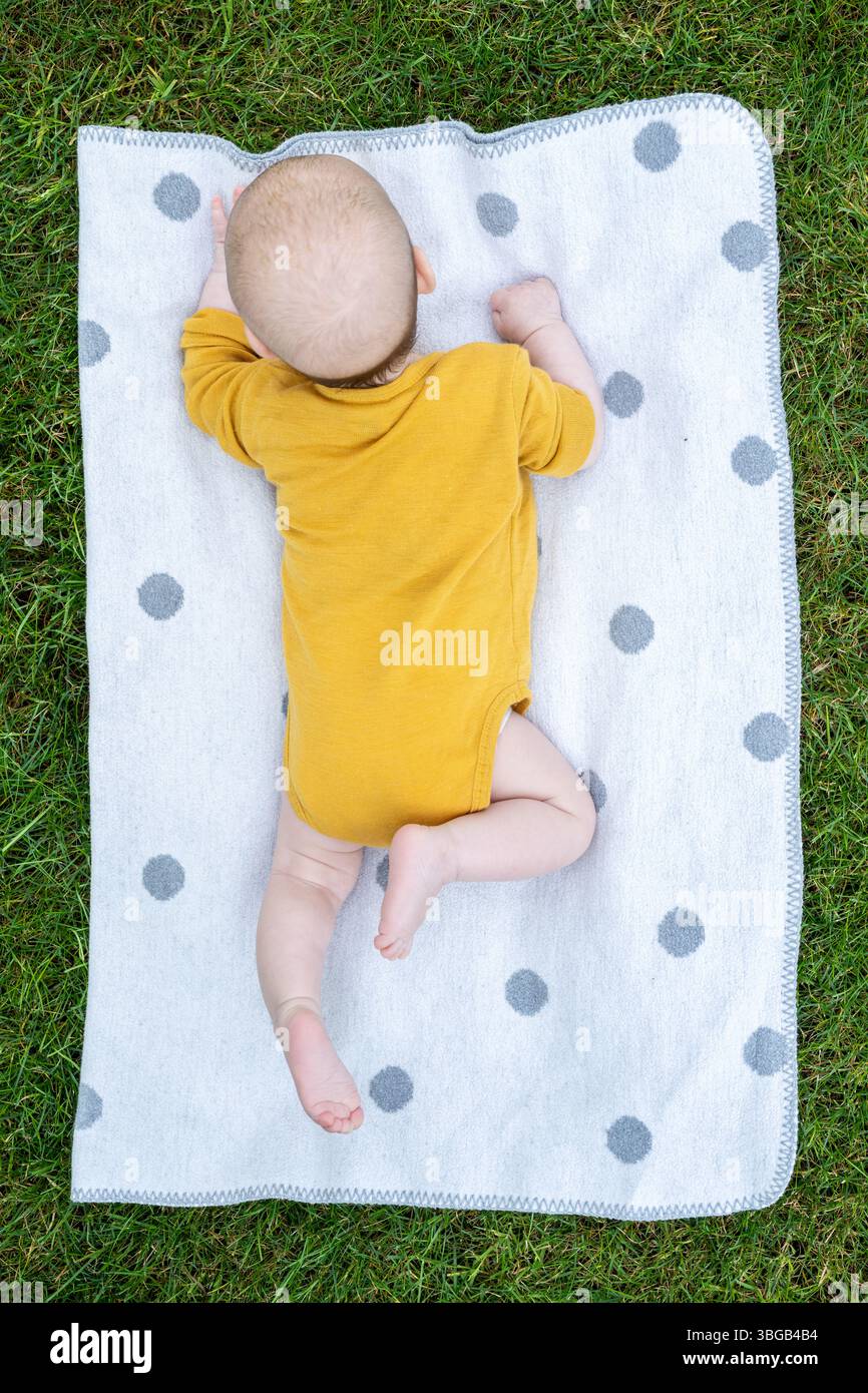Beschreibung: Baby auf Polka Dot Blanket: Ein wertvolles Baby liegt auf seinem Bauch auf einer weichen Polka Dot Decke auf einem leuchtend grünen Rasen und erkundet die Welt aro Stockfoto Beschreibung: Baby auf Polka Dot Blanket: Ein wertvolles Baby liegt auf seinem Bauch auf einer weichen Polka Dot Decke auf einem leuchtend grünen Rasen und erkundet die Welt aro Stockfoto