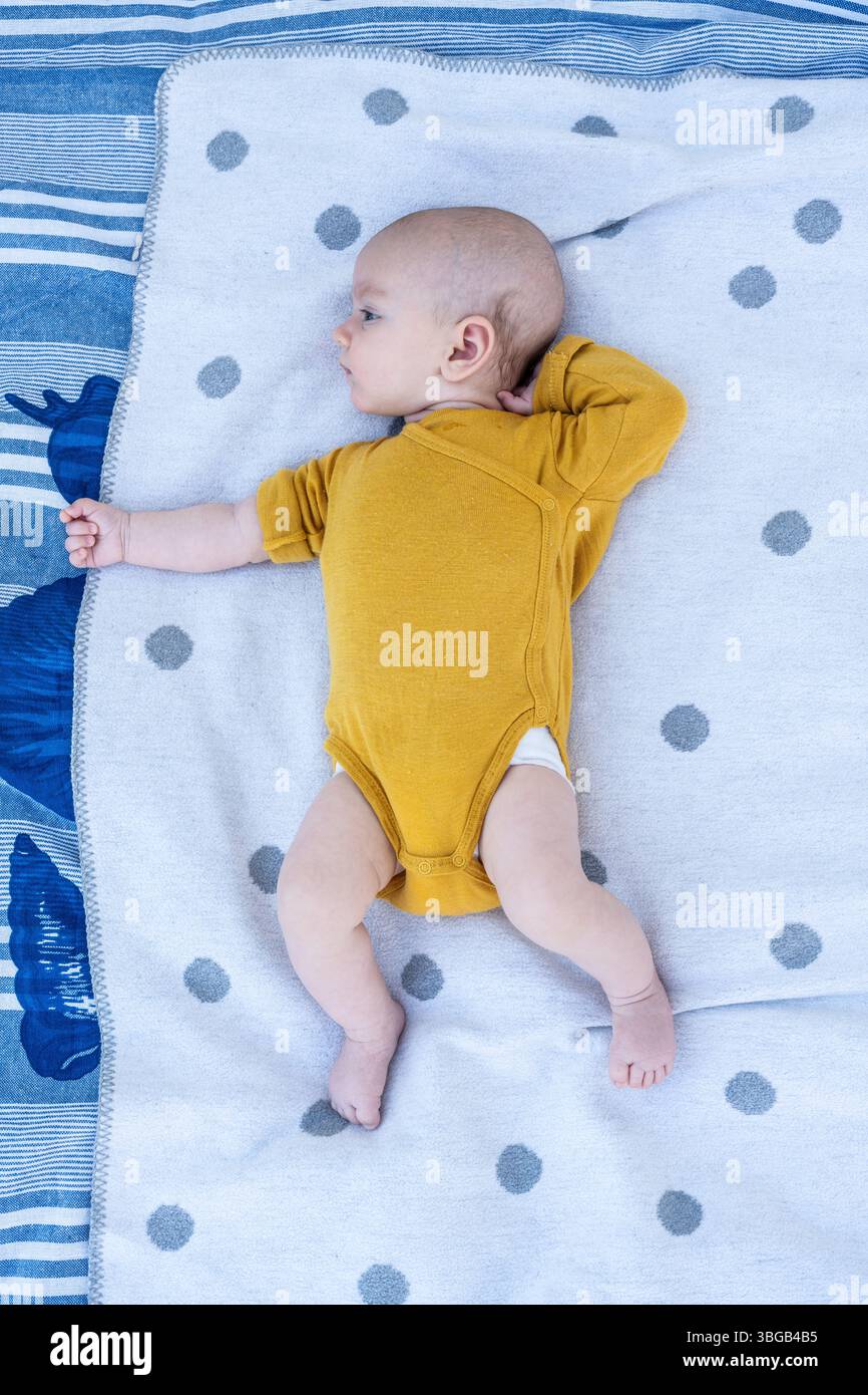 Beschreibung: Golden Slumber: Ein heiterer Top-Down-Schuss zeigt ein Kind in einem sonnigen gelben Einteiler, der friedlich auf einer weichen, mit Polka gepunkteten Decke ruht. Stockfoto Beschreibung: Golden Slumber: Ein heiterer Top-Down-Schuss zeigt ein Kind in einem sonnigen gelben Einteiler, der friedlich auf einer weichen, mit Polka gepunkteten Decke ruht. Stockfoto