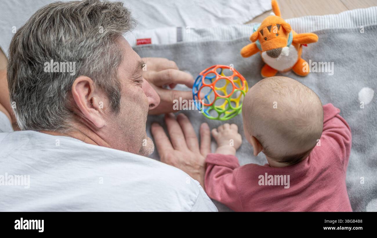 Blick von oben auf die Köpfe eines Großvaters und Enkelkindes, die zusammen mit Babyspielzeug auf einem weichen Boden spielen. Stockfoto Blick von oben auf die Köpfe eines Großvaters und Enkelkindes, die zusammen mit Babyspielzeug auf einem weichen Boden spielen. Stockfoto
