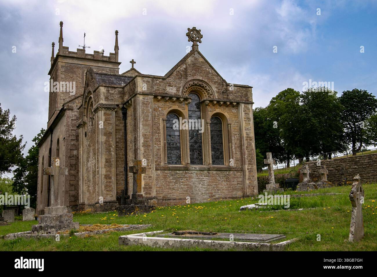 Historische Steinkirche St. Leonard's in Marston Bigot Somerset UK, umgeben von alten Grabsteinen und grünem Laub an einem bewölkten Tag Stockfoto