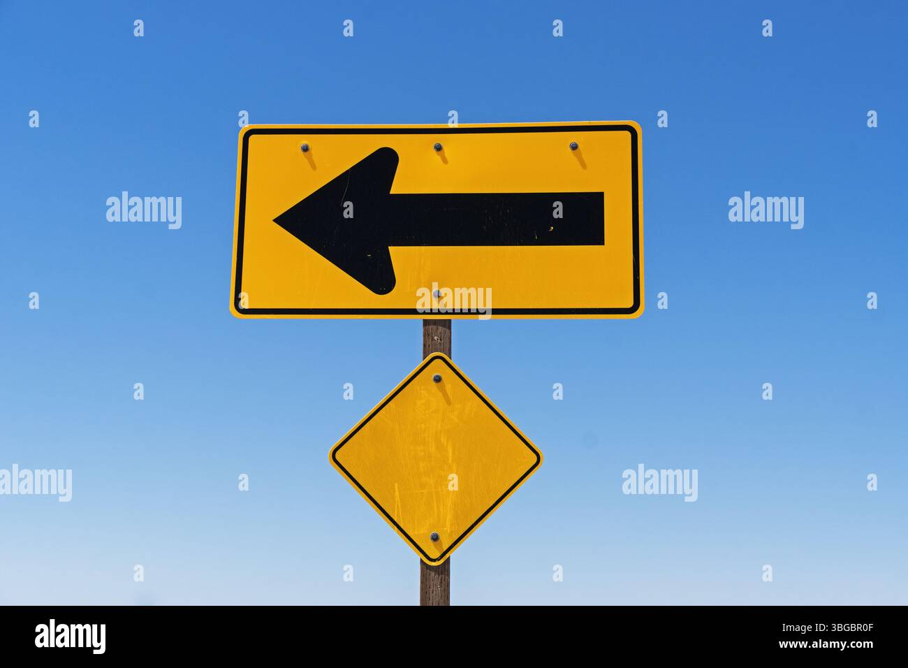 Gelbes und schwarzes reflektierendes Warnschild mit Linkspfeil und Diamantreflektor und blauem Himmel dahinter Stockfoto