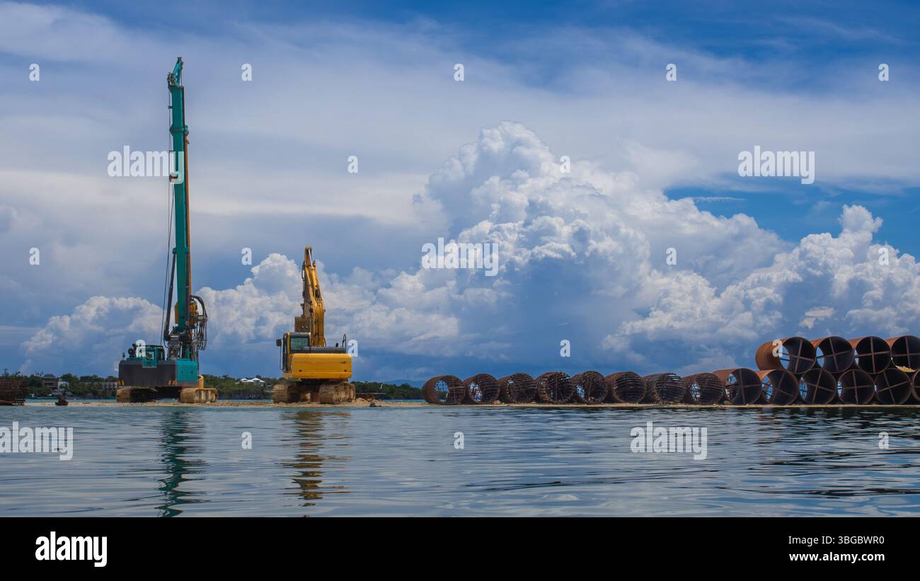 Bagger und Kran, Metallgehäuse mit großem Durchmesser gestapelt. Wunderschöner Hintergrund mit blauem Himmel und Meer Stockfoto