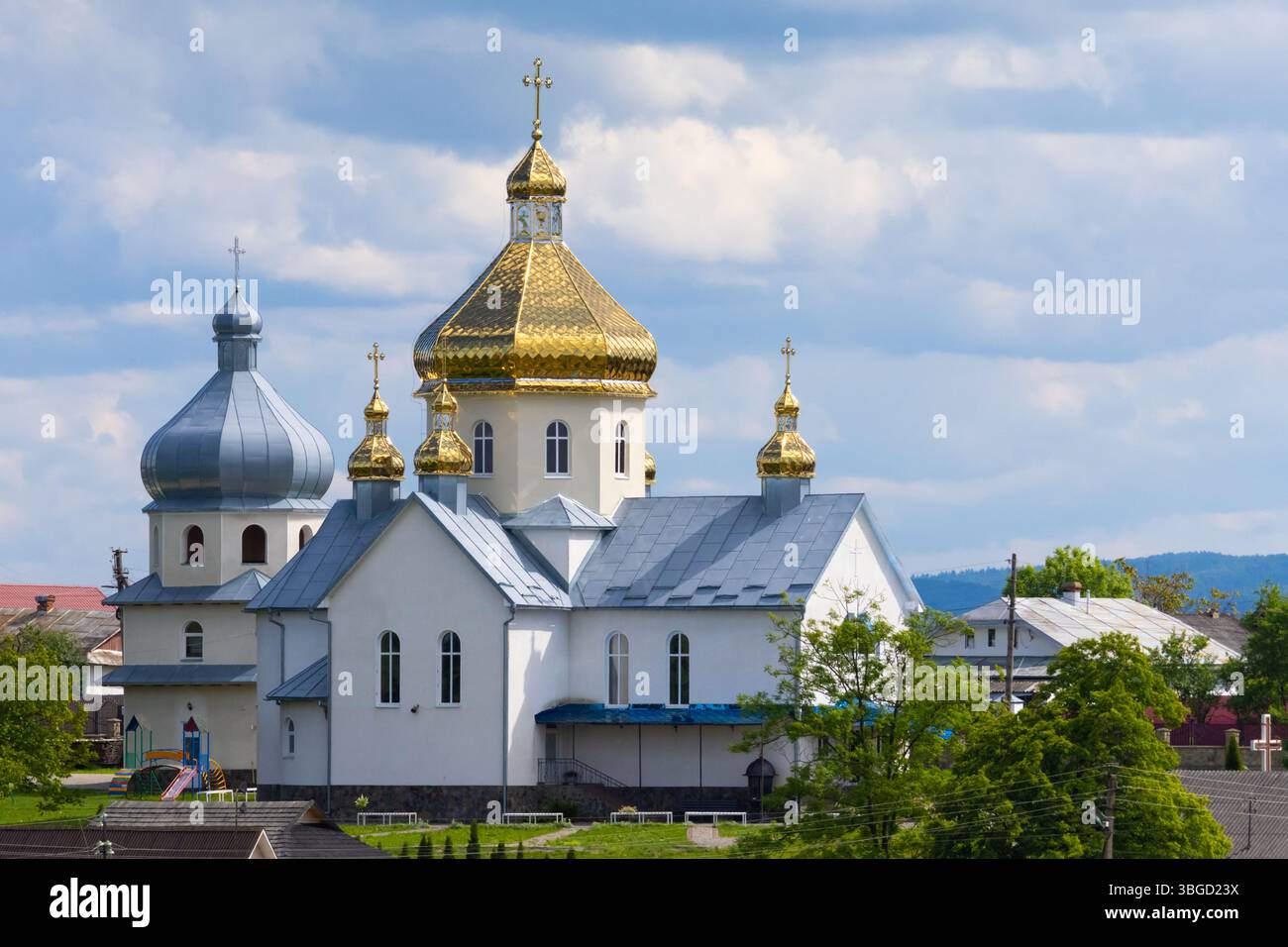 Orthodoxe Kirche mit goldener Kuppel in einem friedlichen ukrainischen Dorf, umgeben von Bäumen und bewölktem Himmel, das spirituelles Erbe zeigt Stockfoto