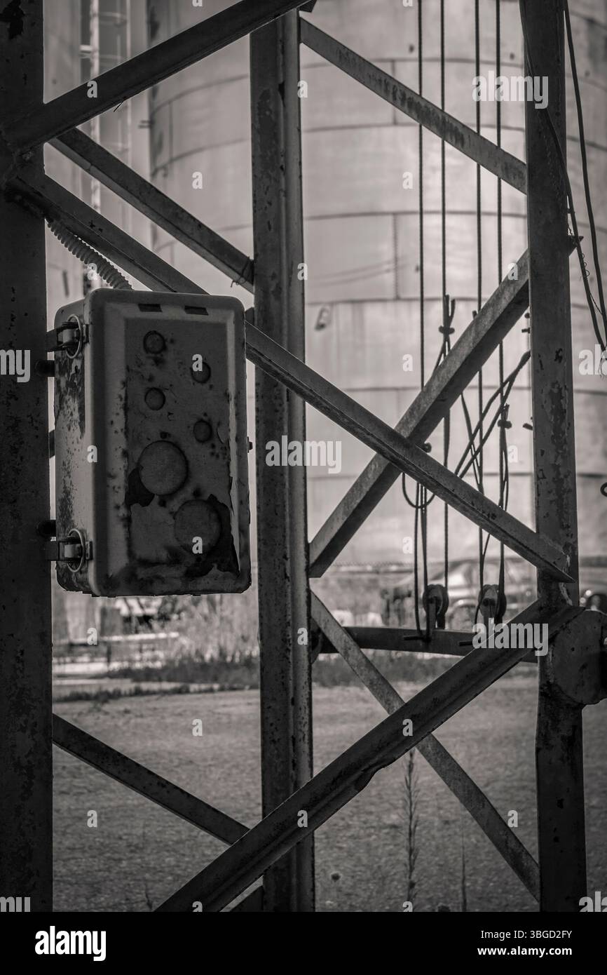 Nahaufnahme eines verwitterten Schaltkastens, der an einem Metallgerüst befestigt ist, mit einem Industriesilo im Hintergrund, das ein Gefühl von Zerfall und abando vermittelt Stockfoto