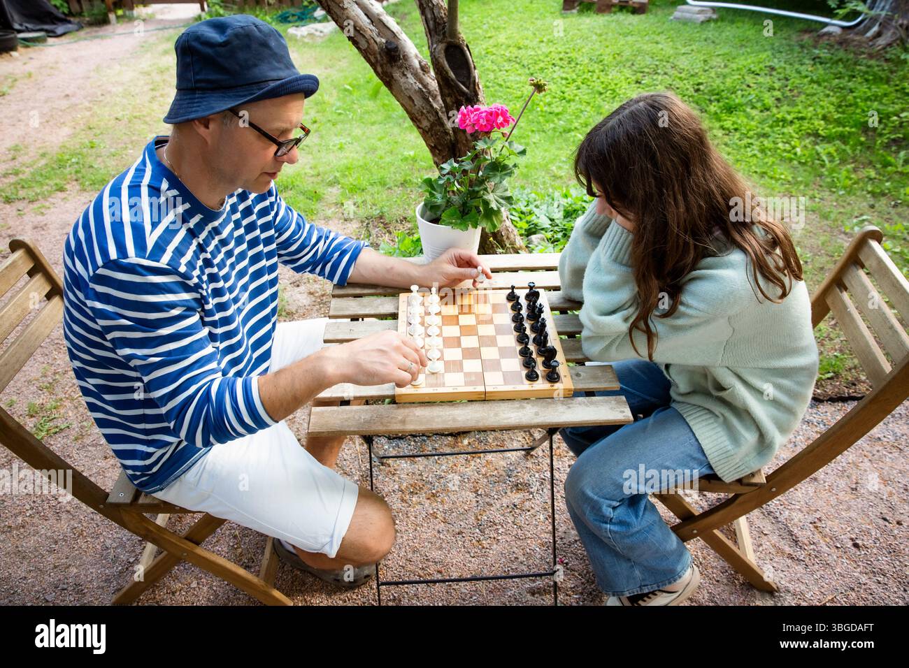 Vater und Tochter spielen Schach in ihrem Garten an einem Sommertag. Hochwertige Familienzeit und mentale Entwicklung in entspannter Atmosphäre im Freien. Stockfoto