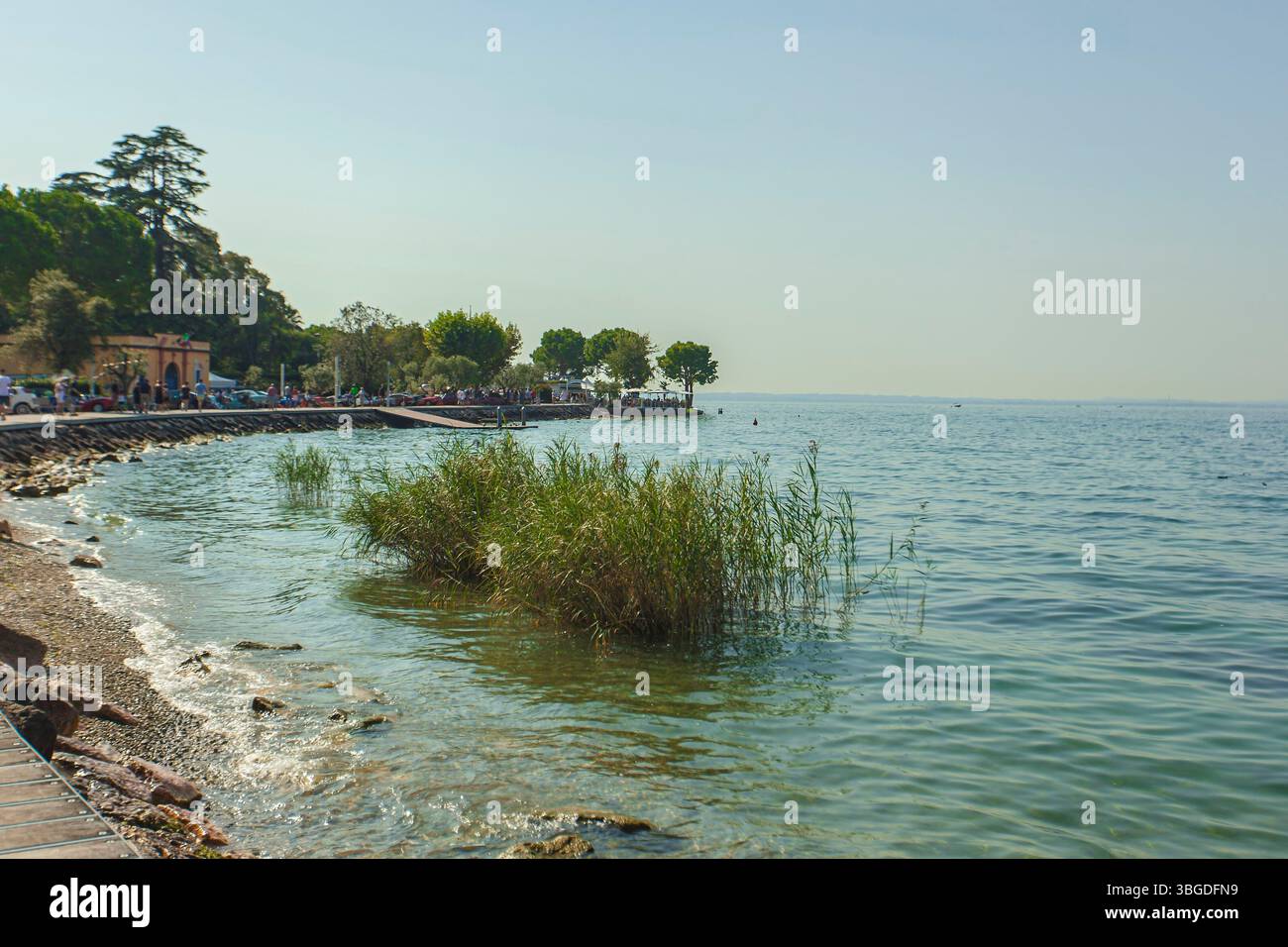 Gardasee, Italien 3. Januar 2025: Ruhiges Wasser, das sanft an einem sonnigen Sommertag am gardasee über das Ufer plätschert, während Touristen die Promena am See genießen Stockfoto
