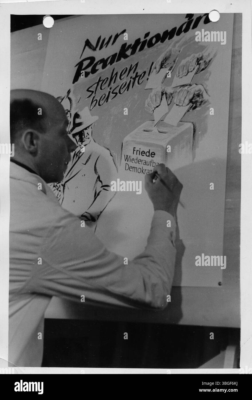 Ein Grafiker fertigt ein Wahlplakat mit der Aufschrift „nur reaktionäre stehen beiseite!“ an, das eine Wahlurne mit den Worten „Friede, Wiederaufbau, Demokratie“ zeigt. Stockfoto