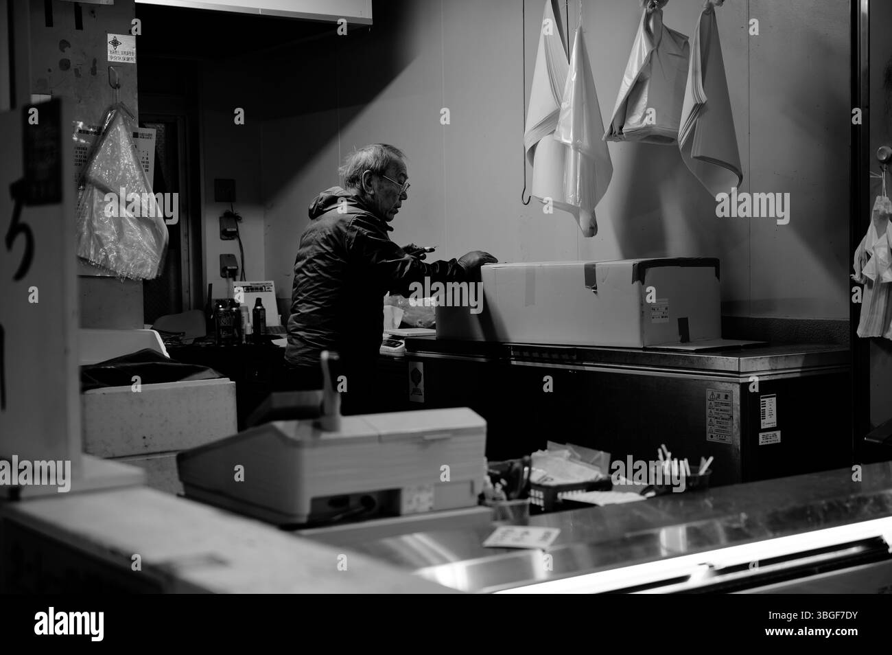 Ein älterer Arbeiter packt sich nach Stunden auf einem schwach beleuchteten Fischmarkt ein Stockfoto