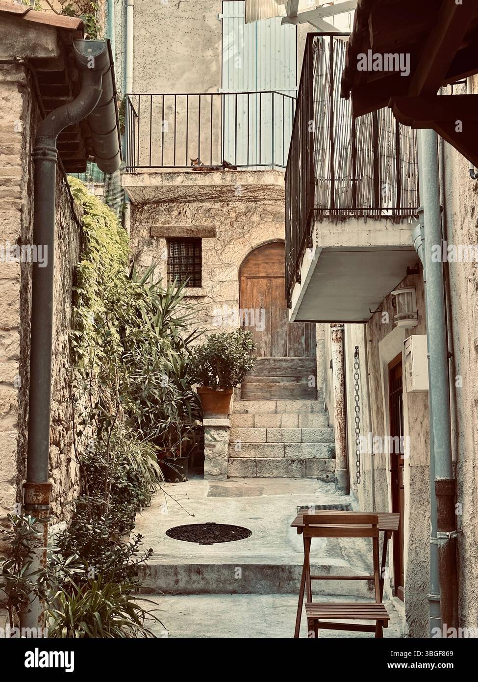 Charmante Gasse in einem mediterranen Dorf mit Steinmauern, Treppen und rustikalen Möbeln, die an einen ruhigen Alltag erinnern. Stockfoto