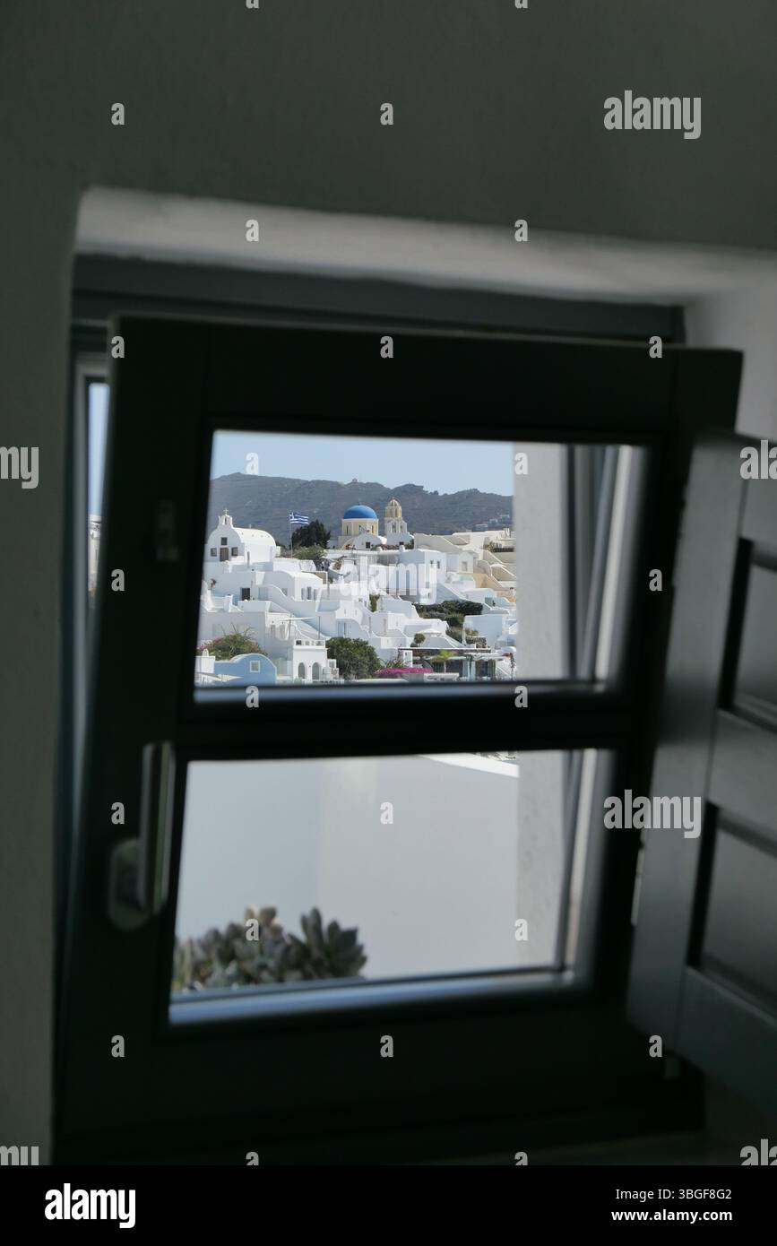 Blick auf Santorini, eingerahmt durch ein Fenster, mit berühmten weißen Gebäuden und blauen Kuppeln an einem sonnigen Tag. Stockfoto