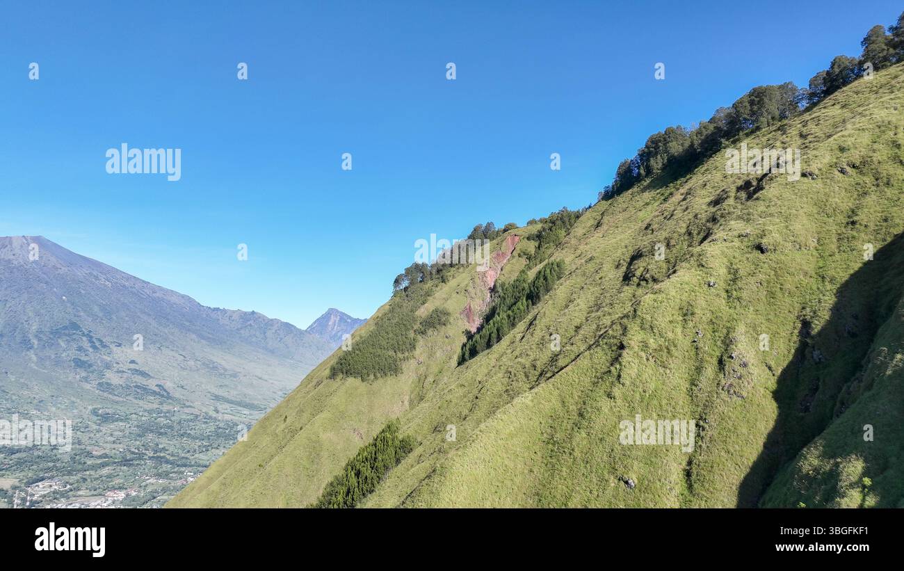 Von Sembalun aus erstreckt sich der Blick über steile, grasbewachsene Hügel bis zu entfernten Vulkangipfeln. Die unberührte Landschaft ist perfekt für Wanderungen und Naturliebhaber Stockfoto