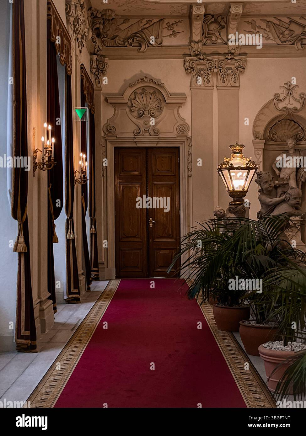 Eleganter Palast oder Museumsinnenraum mit klassischer Architektur, rotem Teppich, kunstvollen Kronleuchtern, Holztüren und Skulpturen. Stockfoto