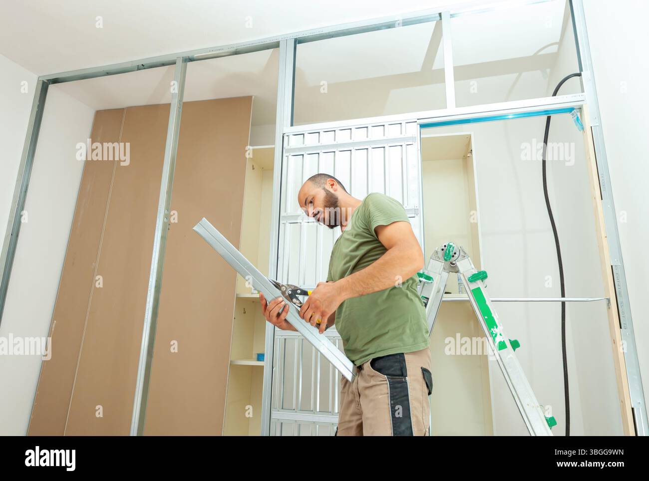 Handwerker schneiden Metallprofile für die Installation von Gipskartonwänden in einem Haus, das gerade renoviert wird, und verwenden Metallbolzen und -Schienen, um Präzision in Konstruktion und Design zu gewährleisten Stockfoto