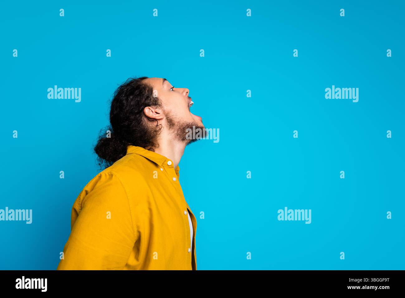 Stilvoller junger Mann in gelbem Hemd, der sich dynamisch und ausdrucksstark vor leuchtendem blauem Hintergrund posiert Stockfoto