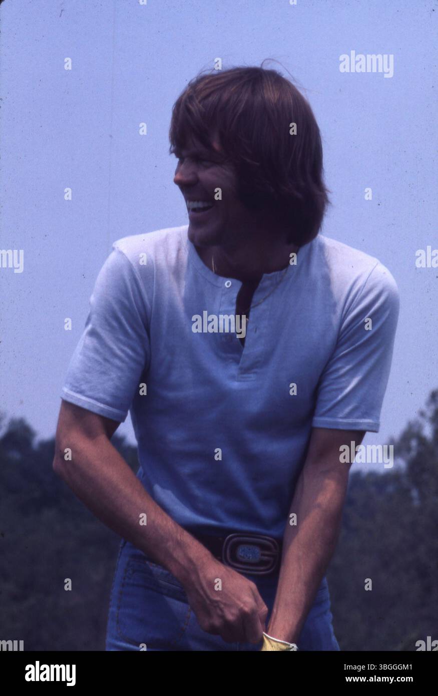 Glen Campbell nimmt 1977 am Memorial Tournament pro-am im Muirfield Village Golf Club Teil, zusammen mit Jack Nicklaus, Gerald Ford, Roger Maltbie, Jackie Gleason, und Bob Hope. Die Zuschauer beobachten von hinten, wie Campbell während der Veranstaltung einen Schuss trifft. Stockfoto