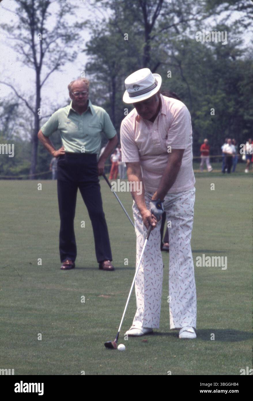 Schauspieler Bob Hope bereitet sich darauf vor, seinen Golfball während des Memorial Tournament Pro-am 1977 im Muirfield Village Golf Club zu schlagen, wobei der ehemalige Präsident Gerald Ford in der Nähe steht. Stockfoto