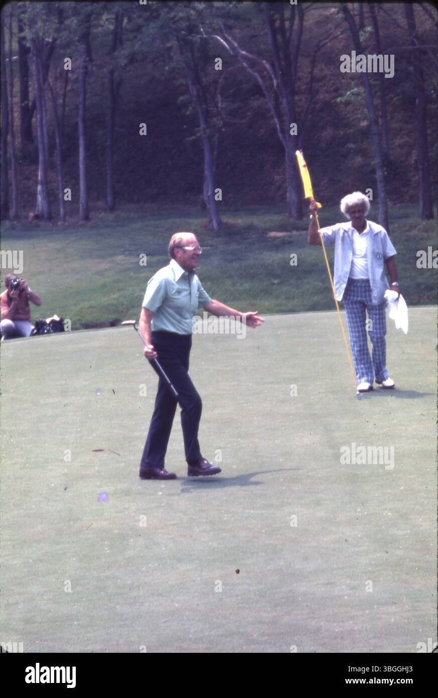 Der ehemalige Präsident Gerald Ford geht während des Memorial Tournament Pro-am 1977 im Muirfield Village Golf Club auf das Grün. Jack Nicklaus' Caddie Angelo Argea hält den Fahnenstock, während ein Fotograf ein Foto macht. Ford spielte in einem Sixsome mit Jack Nicklaus, Roger Maltbie, Bob Hope, Jackie Gleason und Glen Campbell. Stockfoto