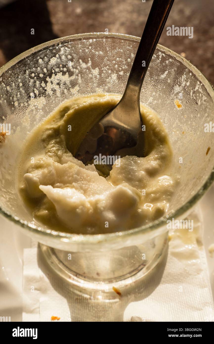 Schmelzende sizilianische Granita mit sichtbarer Textur und Löffel im Glasbecher. In natürlichem Licht, Konzept der Sommererfrischung und authentischer Geschmack Stockfoto