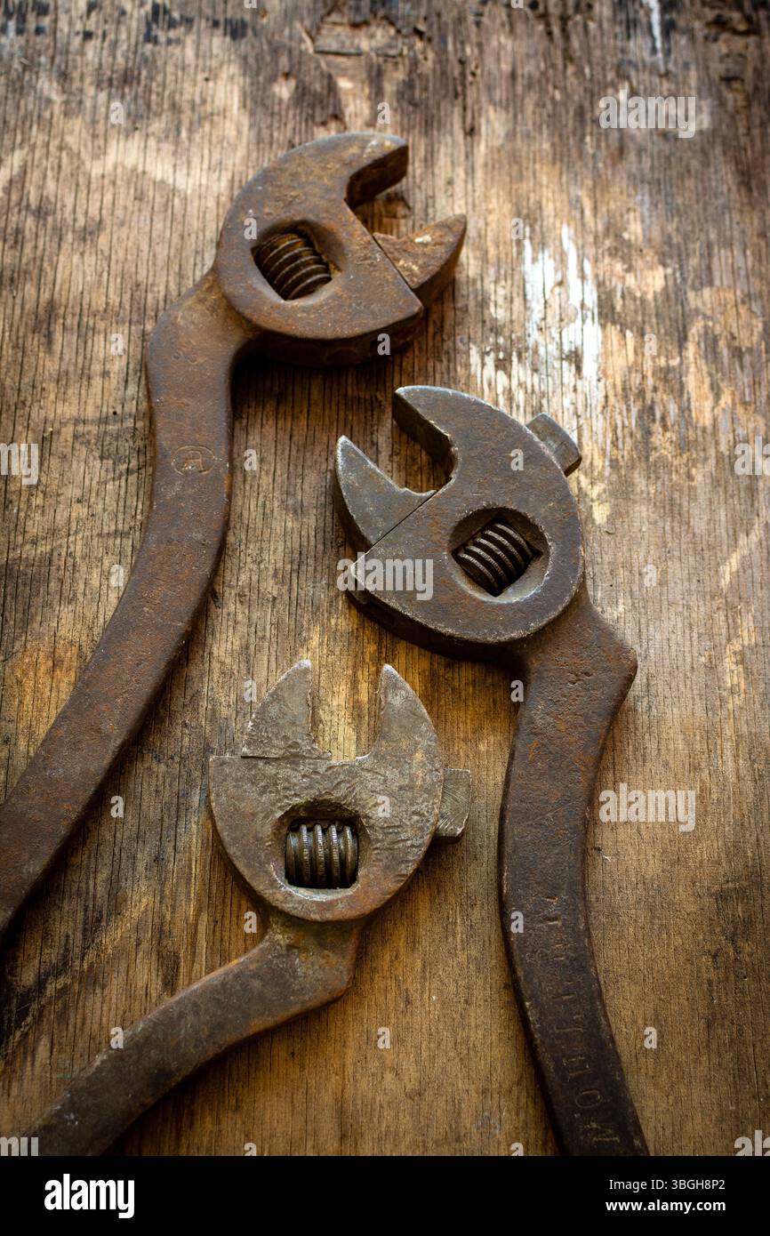 Drei antike verstellbare Schraubenschlüssel ruhen auf einem verwitterten Holztisch und betonen ihr einzigartiges Design und ihre robuste Konstruktion. Stockfoto
