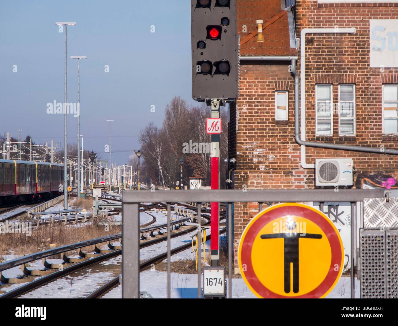 Absperrgitter am Ende eines Bahnsteigs mit Piktogramm mit Stellwerk, Gleisen und rotem Ausstiegssignal dahinter. Stockfoto