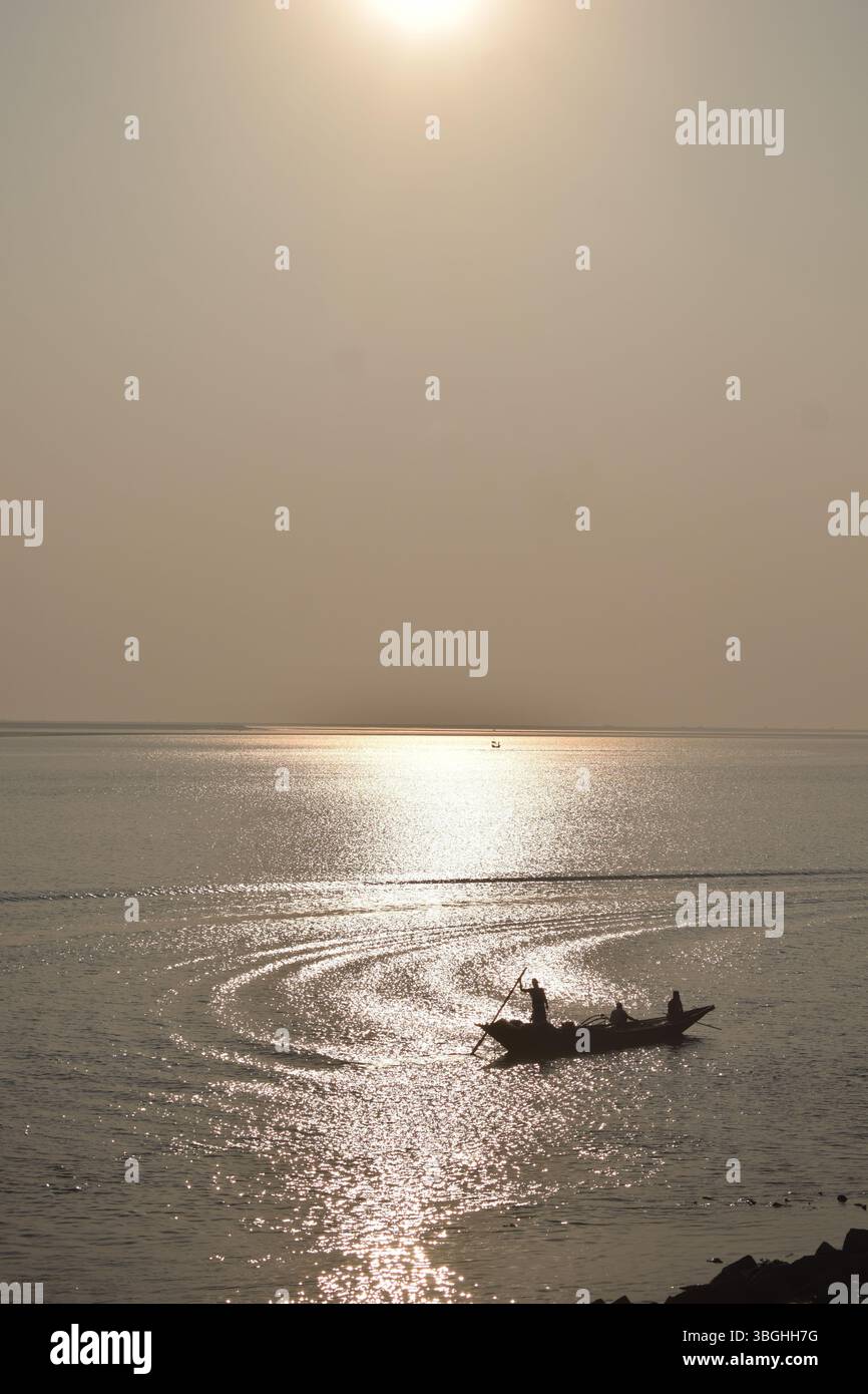 Ein Boot, das auf den goldenen Gewässern des Meghna River driftet und das Wesen des Lebens eines Fischers bei Sonnenuntergang festlegt. Stockfoto
