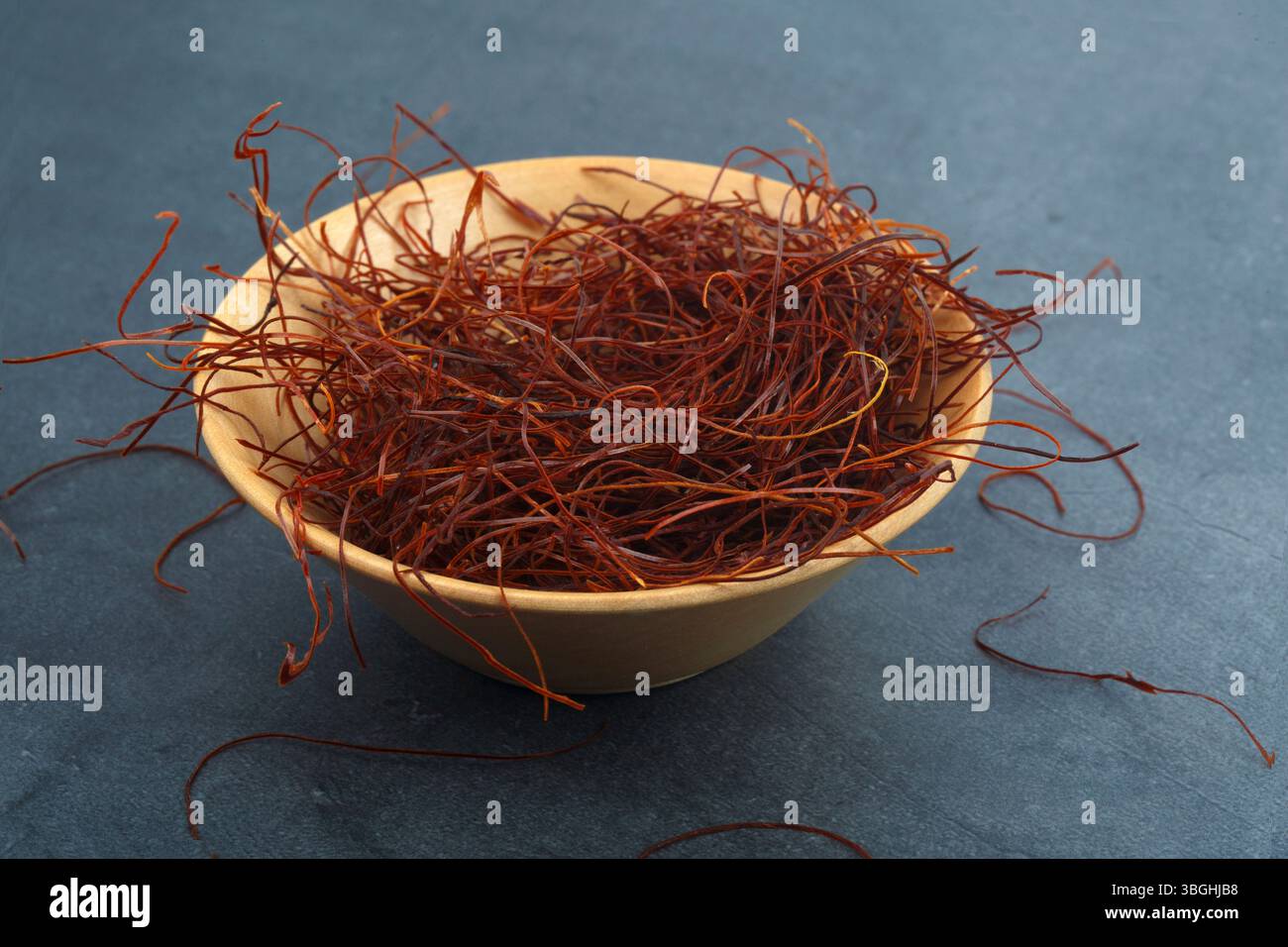 Rote, heiß getrocknete Chilifäden in einer winzigen Holzschale isoliert auf dunklem Hintergrund Stockfoto